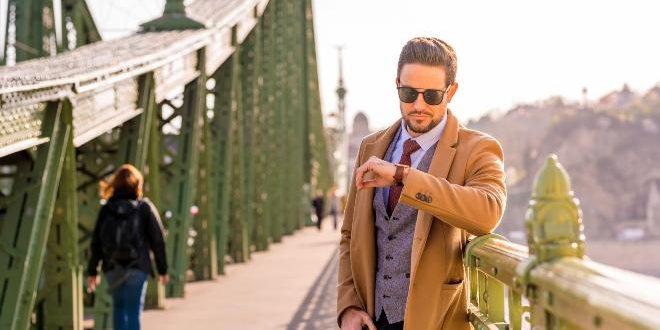 An elegant man standing on a bridge and checking the time.