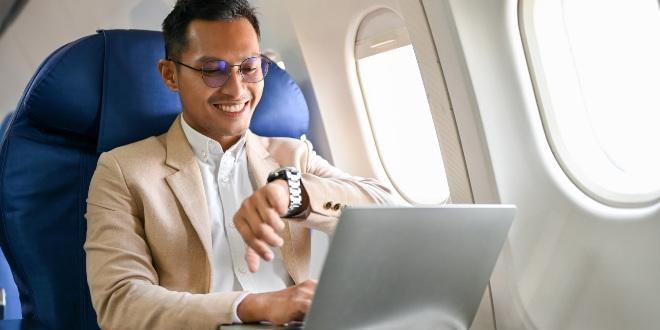 Successful and smart businessman sits at the window seat in business class, checking his watch for the arrival time, on the flight for his business trip.